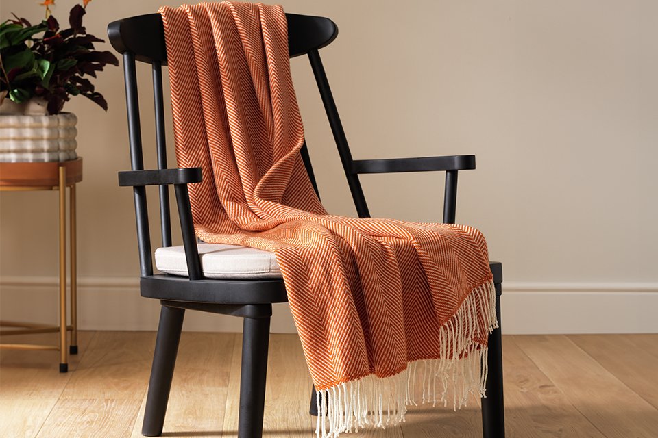 HAB Herringbone Throw in burnt orange colour draped over an armchair.